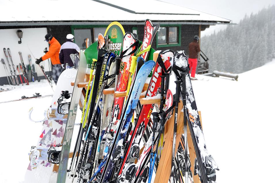 Skiregal mit verschiedenen Skiern und Snowboard im Schnee vor einer Berghütte an einem bewölkten Tag.