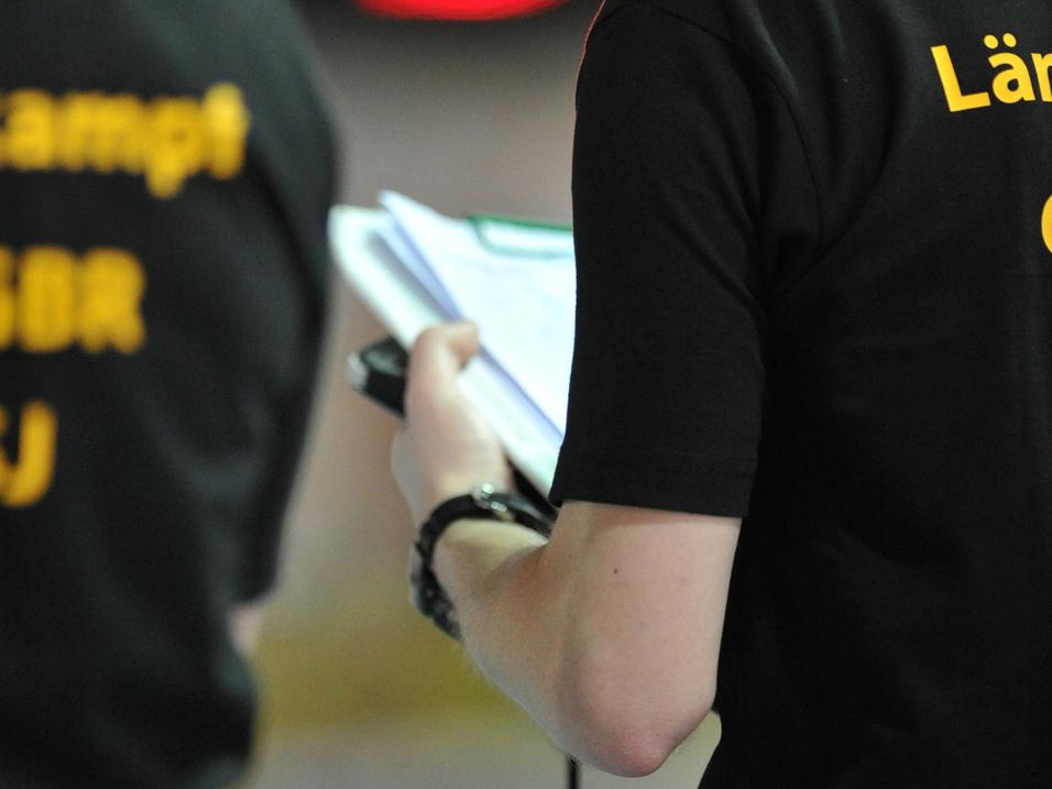 Person in schwarzem T-Shirt hält ein Notizbuch und Stift, im Hintergrund leuchtende Ampeln.