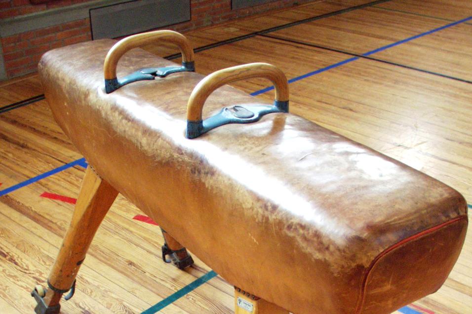 Turnbank mit Holzgriffen auf einem Holzfußboden in einer Sporthalle.